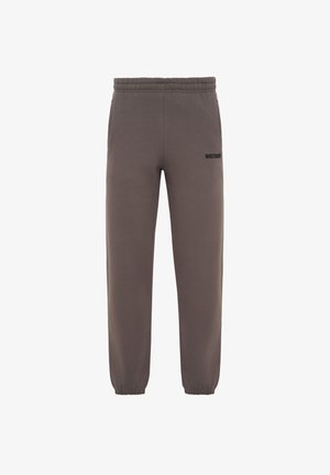 Pantalon de jogging marron avec taille et chevilles élastiques, petit texte noir sur la partie supérieure de la cuisse gauche sur fond blanc.