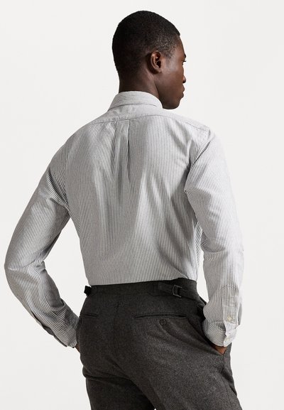 Svītraina krekla ar pogām gaismati pelēkā un baltā krāsā, ar apkakli un pogu aprocēm. Valkāts ar pelēkām biksēm, kurām ir josta un kabatas.