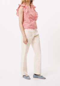Rotes Blumenmusteroberteil mit Rüschen, kombiniert mit hellbeigen Hosen. Das Model trägt hellblaue flache Schuhe. Einfaches, lässiges Outfit.