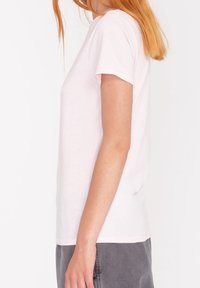 Ruusunpunainen, lyhythihainen puuvillainen t-paita, jossa on klassinen pyöreä pääntie ja suora istuvuus, yhdistetty harmaisiin housuihin.