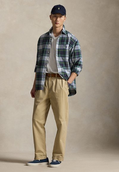 Plaid button-up shirt in green, blue, and white, layered over a white V-neck T-shirt; beige chinos and navy sneakers complete the outfit.