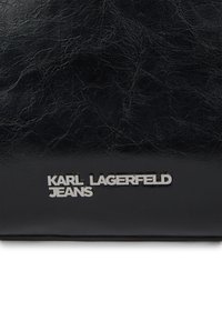 Μαύρη υφασμάτινη επιφάνεια από δέρμα με ασημένιο λογότυπο "KARL LAGERFELD JEANS" σε κεφαλαία γράμματα κοντά στο κάτω κέντρο.