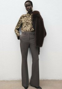Brown pinstripe trousers paired with an olive leopard print blouse and a dark fur shawl, featuring pointed black heels and gold earrings.