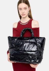 Borsa tote nera e morbida realizzata in materiale lucido, con un design trapuntato, manici doppi e logo visibile sul davanti.