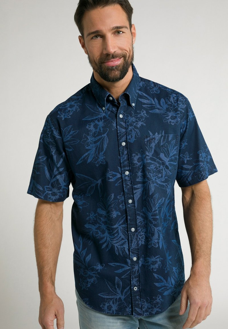 Korte mouwen, button-up shirt in donker marineblauw met een textuurpatroon van bloemen in lichter blauw. Heeft een borstzak en een kraag.