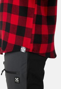 Rood en zwart geblokt shirtstof met een label; gecombineerd met grijze broek met zakken en een logo-patch op de dij.