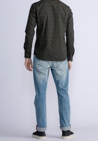 Camicia nera con un piccolo motivo geometrico, abbinata a jeans azzurri chiari con una finitura sbiadita e risvolti. Sneakers nere con suola bianca.