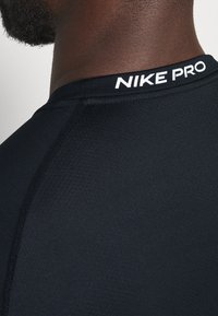 Černé sportovní tričko Nike Pro s hladkým povrchem, těsným střihem a bílým logem značky na límci.