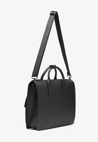 Bolso de cuero negro con dos asas superiores y una correa de hombro desmontable. Presenta una forma rectangular elegante y una textura suave.