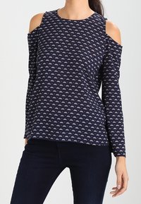 Navy long-sleeve top with cold shoulder cutouts, featuring a repeated geometric pattern in light colors and a rounded neckline.