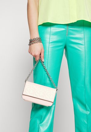 Piccola borsa a mano rosa con motivo in rilievo, tracolla a catena argentata, forma rettangolare, abbinata a pantaloni in pelle verde e top giallo.