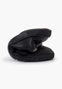 Chaussure noire flexible pliée en deux, avec semelle texturée et sangle Velcro, mettant en avant son design pliable et compact sur fond blanc.