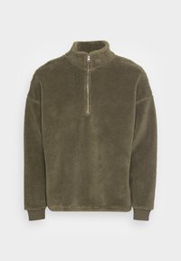 Pile verde oliva con colletto alto, chiusura con mezza cerniera e polsini a costine. Texture morbida e vestibilità comoda per il massimo comfort.