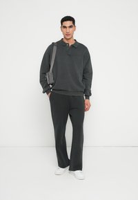 Czarnoszary, oversize'owy sweter z kołnierzem, w zestawie z dopasowanymi szarymi spodniami. Modelka nosi torbę na ramię i białe trampki.