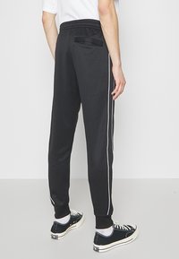 Svarta atletiska joggers med slim fit, elastisk midja och vita sidosträck; har en bakficka och en mjuk textur.