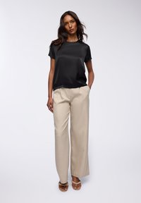 Top corto in satin nero a maniche corte abbinato a pantaloni a gamba larga beige chiaro. I pantaloni presentano una leggera texture; il modello indossa sandali con cinturini color nocciola.