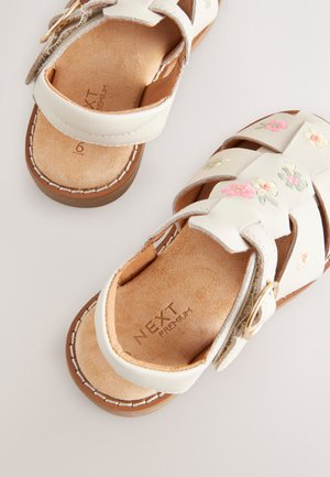 Weiße Ledersandalen mit Blumenstickerei in Rosa und Grün. Mit verstellbarem Riemen und gepolsterter Innensohle sowie brauner Sohle.