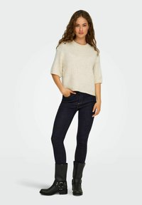 Lys beige strikket sweater med korte ærmer, parret med mørkeblå slim-fit jeans og sorte læder ankelstøvler med hardware-detaljer.