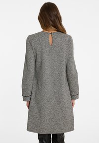 Grau gesprenkelter Mantel mit einer lockeren Passform, Ellenbogen-langen Ärmeln und einem Schlüsselloch-Ausschnitt im Rücken. Akzentuiert mit schwarzem Piping an den Manschetten.