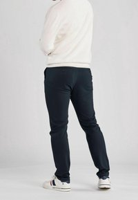 Námořnické modré kalhoty s úzkým střihem, které mají dvě zadní kapsy a hladkou texturu. Nosit s bílým svetrem a bílými teniskami.