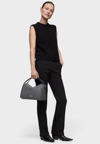 Czarna bezrękawnikowa bluzka, dopasowane czarne spodnie i szara torebka w wzory z zaokrąglonymi krawędziami i górnym uchwytem; na stopach czarne buty na szpic.