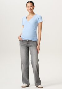Lysblå omslagstop med kortærmer, parret med grå flagrende jeans og hvide sko. Enkel design med en glat tekstur.