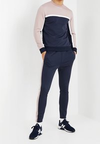 Chándal deportivo en azul marino y rosa con un diseño de bloques de color, que incluye un escote redondo, mangas largas y pantalones ajustados. Zapatillas negras.