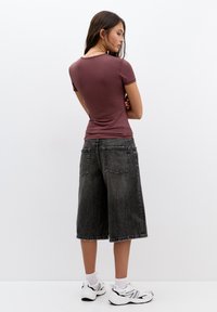 Un top scurt, mărime ajustată, de culoare vișinie, asortat cu pantaloni scurți din denim negri, lejeri, până la genunchi. Tenisi albi cu accente negre completează ținuta.