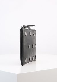 Mustat nahkainen clutch-kotelo, jossa on tyylikäs muotoilu, pyöreitä metallisia yksityiskohtia, sileä pinta ja vetoketjukiinnitys kankaisella vedolla.