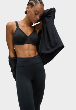 Zwarte sportbeha met netdetail, verstelbare bandjes en naadloze cups, gecombineerd met zwarte high-waisted leggings met een gladde textuur.