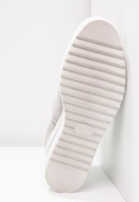 Harmaa mokkanahkasaappi, jossa on teksturoitu valkoinen kumipohja, jossa on vaakasuorat urat ja pyöristetty varvas. Siisti, minimalistinen muotoilu.