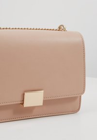 Borsa a mano in pelle rosa chiaro con forma rettangolare, hardware dorato e tracolla a catena. Presenta una chiusura piatta sul davanti. Texture liscia.