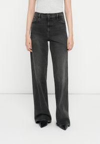 Zwarte wijde jeans van denim, met een hoge taille, vervaagde afwerking en klassiek vijf-pocket ontwerp. Gecombineerd met puntige zwarte schoenen.