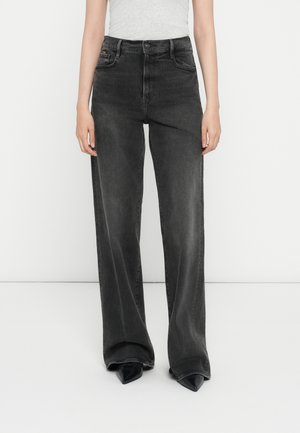 Zwarte wijde jeans van denim, met een hoge taille, vervaagde afwerking en klassiek vijf-pocket ontwerp. Gecombineerd met puntige zwarte schoenen.