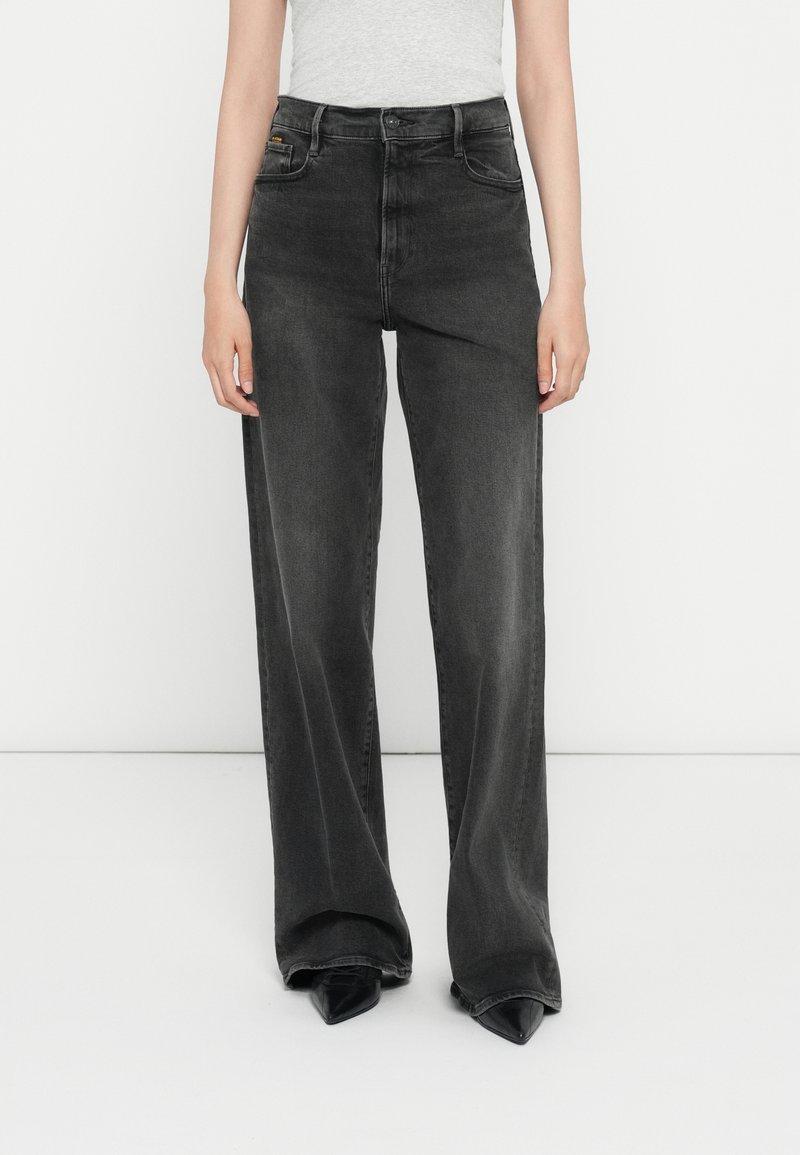 Zwarte wijde jeans van denim, met een hoge taille, vervaagde afwerking en klassiek vijf-pocket ontwerp. Gecombineerd met puntige zwarte schoenen.