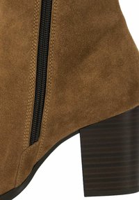 Bottine en suède marron avec une fermeture éclair latérale, dotée d'un talon en bois marron texturé et d'un détail de fermeture éclair noir lisse.