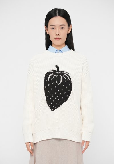 Pull blanc en maille avec un grand motif fraise noire. Comprend des poignets et un ourlet côtelés, une coupe décontractée et un col ouvert porté sur une chemise bleu clair.