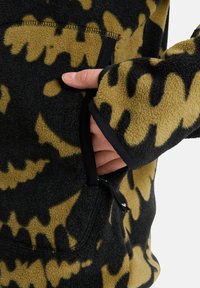 Giacca in fleece con motivo camouflage nero e giallo, dotata di tasca con zip e polsini aderenti con rifiniture nere. Tessuto morbido e materiale caldo.