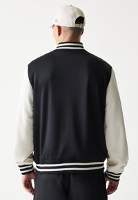 Μαύρο και κρεμ μπουφάν varsity με πλεκτό γιακά και μανσέτες, με μονόχρωμη υφή και ριγέ διακοσμητικά στη ζώνη της μέσης.