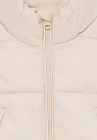 Beige pufferjacka med hög krage, framdragkedja och sydd paneldesign. Slät textur med minimala designdetaljer.