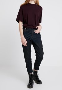 Musta tiukka housut, joissa on kerätty rakenne nilkoissa, yhdistettynä löyhään, lyhythihaiseen tumman viininpunaisiin t-paitaan ja mustiin sotilaskenkään.