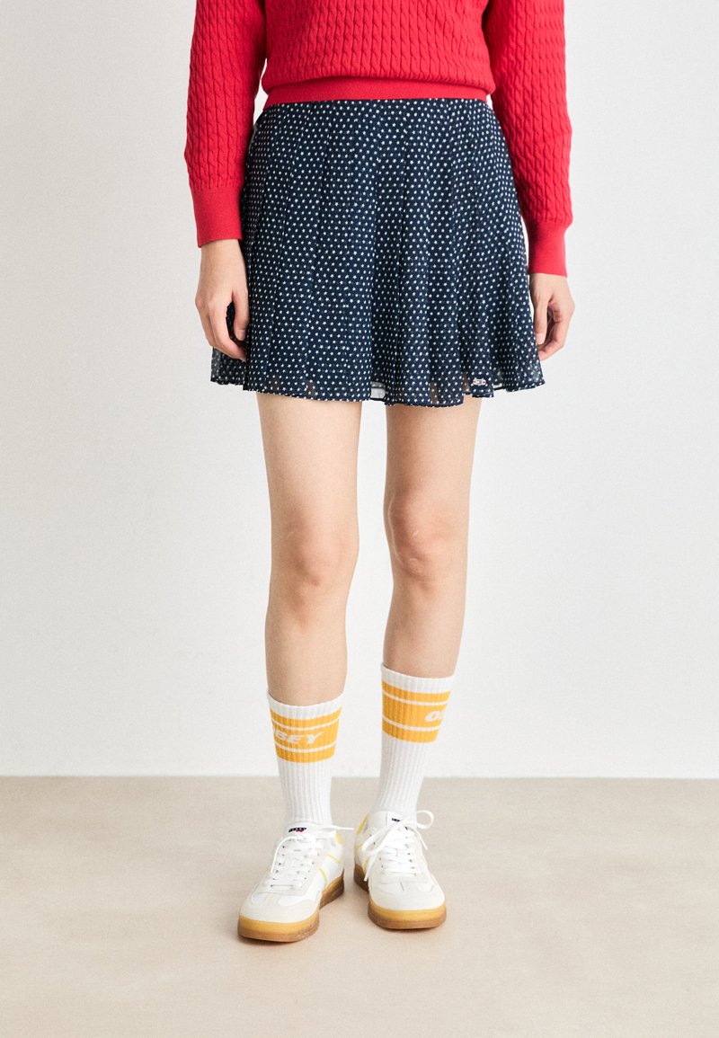 Marineblå prikket skjørt med en utsvakt design, paret med hvite sneakers og sokker med gule striper. Genseren er teksturert og rød.