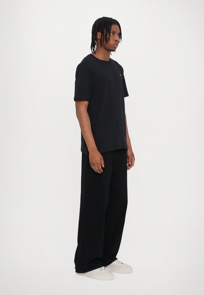 Tricou negru cu croială lejeră, gât rotund și mâneci scurte, asortat cu pantaloni negri cu picioare largi și adidași albi.