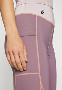 Leggings u prigušenoj lavandi, s kontrastnim breskovim šavovima i glatkom teksturom. Dizajn s visokim strukom i detaljima na bočnim panelima.