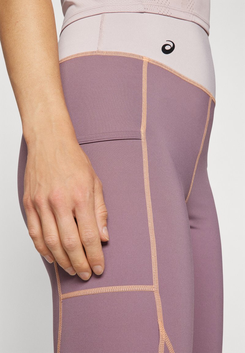 Leggings dans une teinte lavande douce, avec des coutures contrastantes en pêche et une texture lisse. Design taille haute avec des détails de panneaux latéraux.