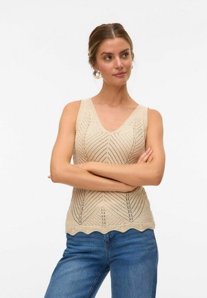 Beige knitted tank top featuring a V-neck, chevron pattern, and scalloped hem, paired with blue jeans. The fabric appears lightweight and textured.
