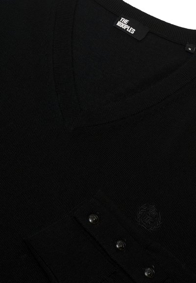 Jersey negro con cuello en V y un bolsillo que cuenta con tres botones negros y un sutil detalle de logo, hecho de una suave tela texturizada.