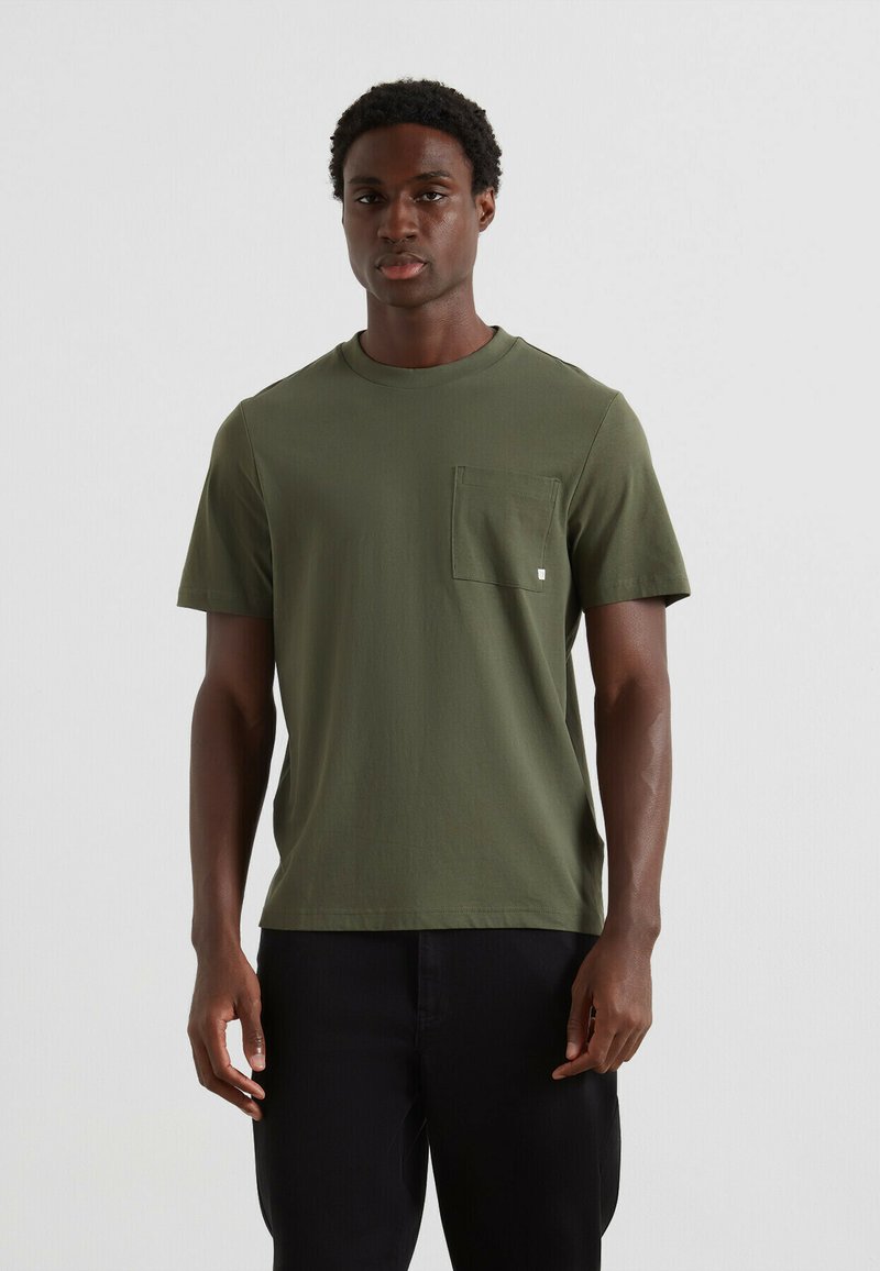 T-shirt en coton vert avec un col rond, des manches courtes et une poche sur le côté gauche de la poitrine. Présente un design minimaliste et une texture douce.