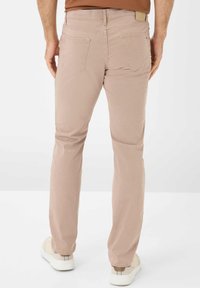Beige slim-fit broeken met een gladde textuur, standaardzakken en een klein merklabel op de achterste tailleband. Draagt bij witte en beige schoenen.
