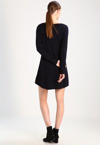 Abito nero a maniche lunghe con un taglio morbido, orlo leggermente svasato e un design in maglia testurizzata. Indossato con stivali neri alla caviglia.
